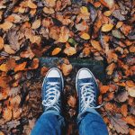 person in blue Converse standing on fall leaves