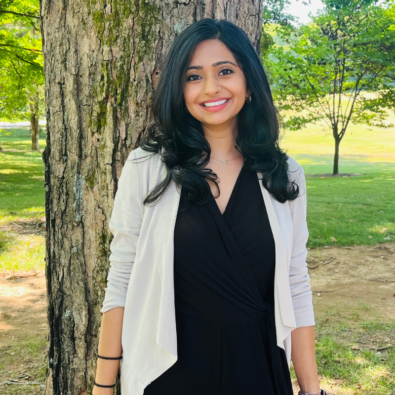 South Asian psychologist Nisha Bhatt stands in front of a tree. 