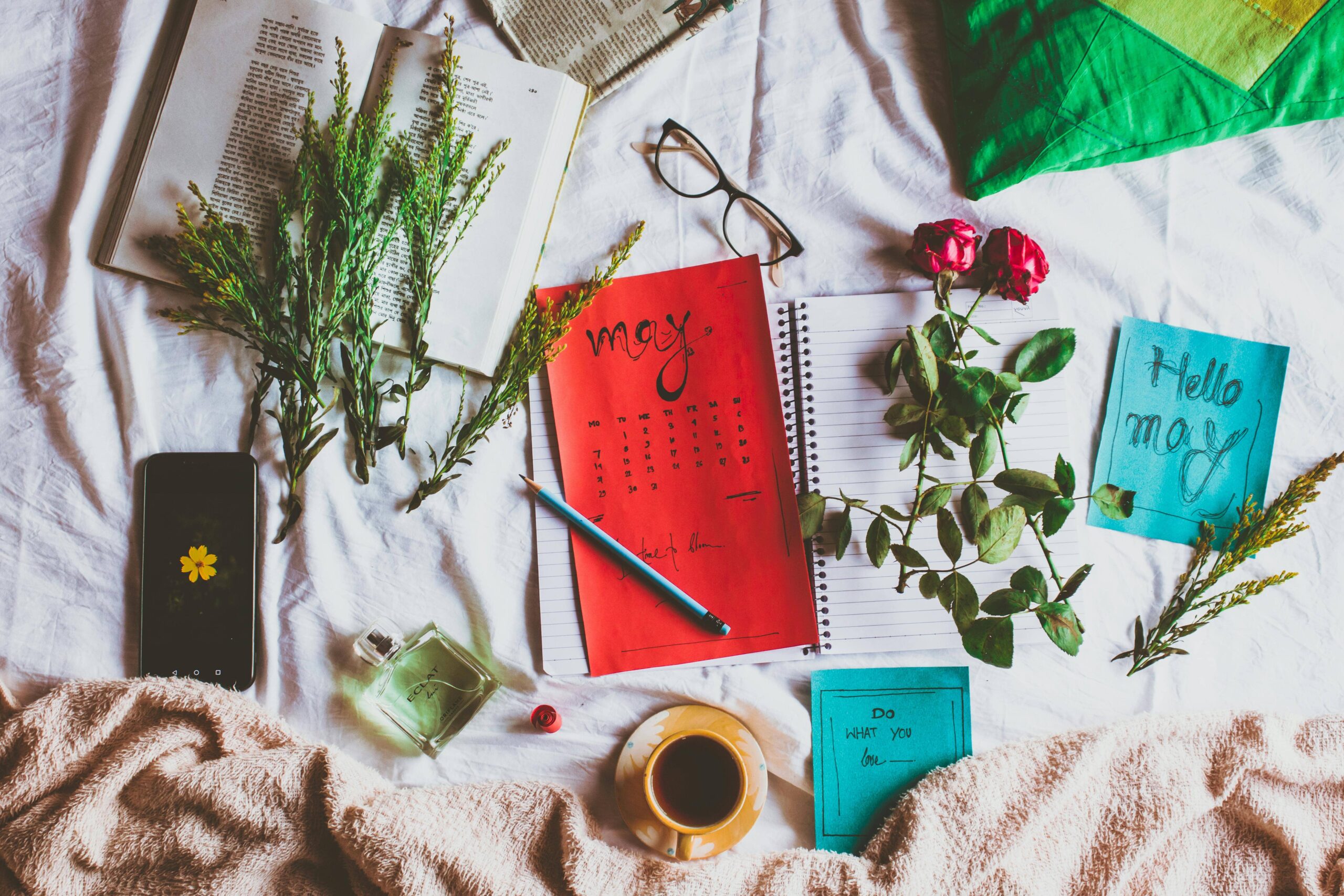 May calendar, coffee, notes, glasses, flowers displayed on a table